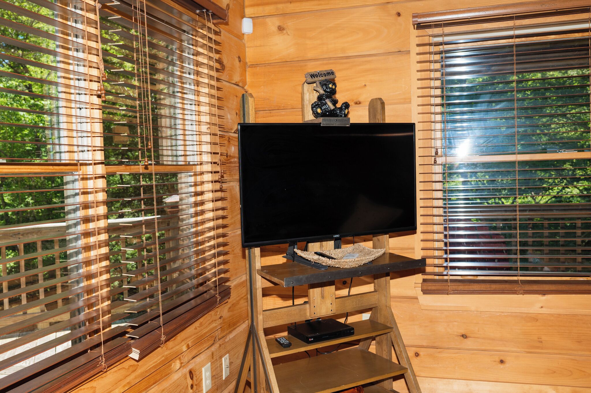A wooden interior with a television on a stand, a welcome sign, and blinds on the windows.