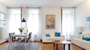 Una sala de estar con un sofá blanco, una mesa de centro, una mesa de comedor con sillas y una lámpara.