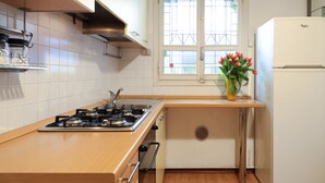 Cocina compacta con estufa a gas, gabinetes blancos, una ventana con vistas y un refrigerador.