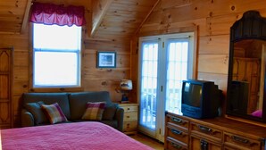 Un ambient acollidor a l'habitació d'una cabana, amb un llit, una petitet i una televisió, i un ventilador de sostre.