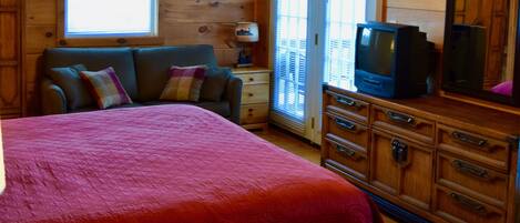 A cozy cabin room with a bed, a dresser, a television, and a ceiling fan.