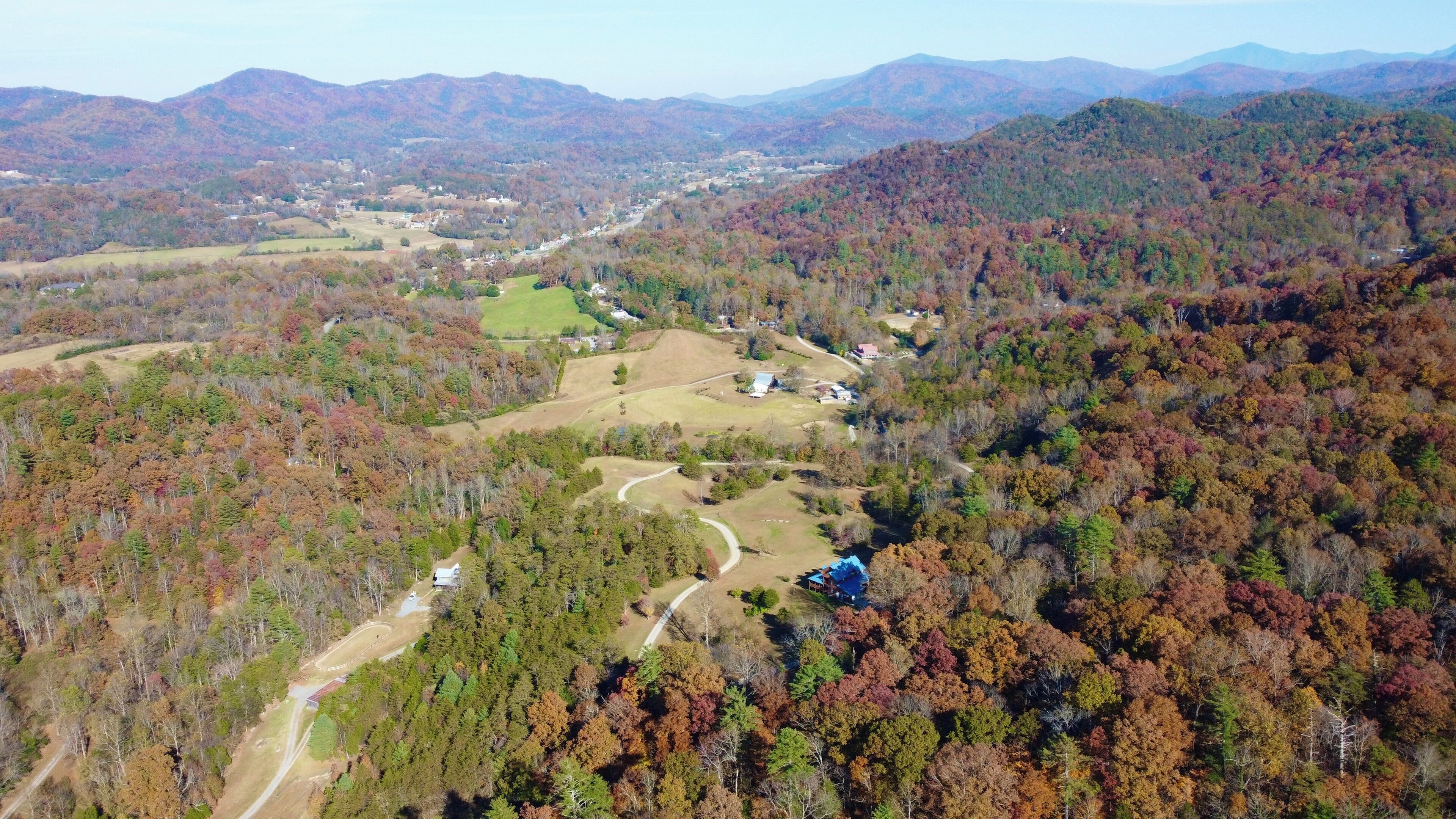An aerial view of a mountainous area with a winding road, scattered buildings, and dense forest.
