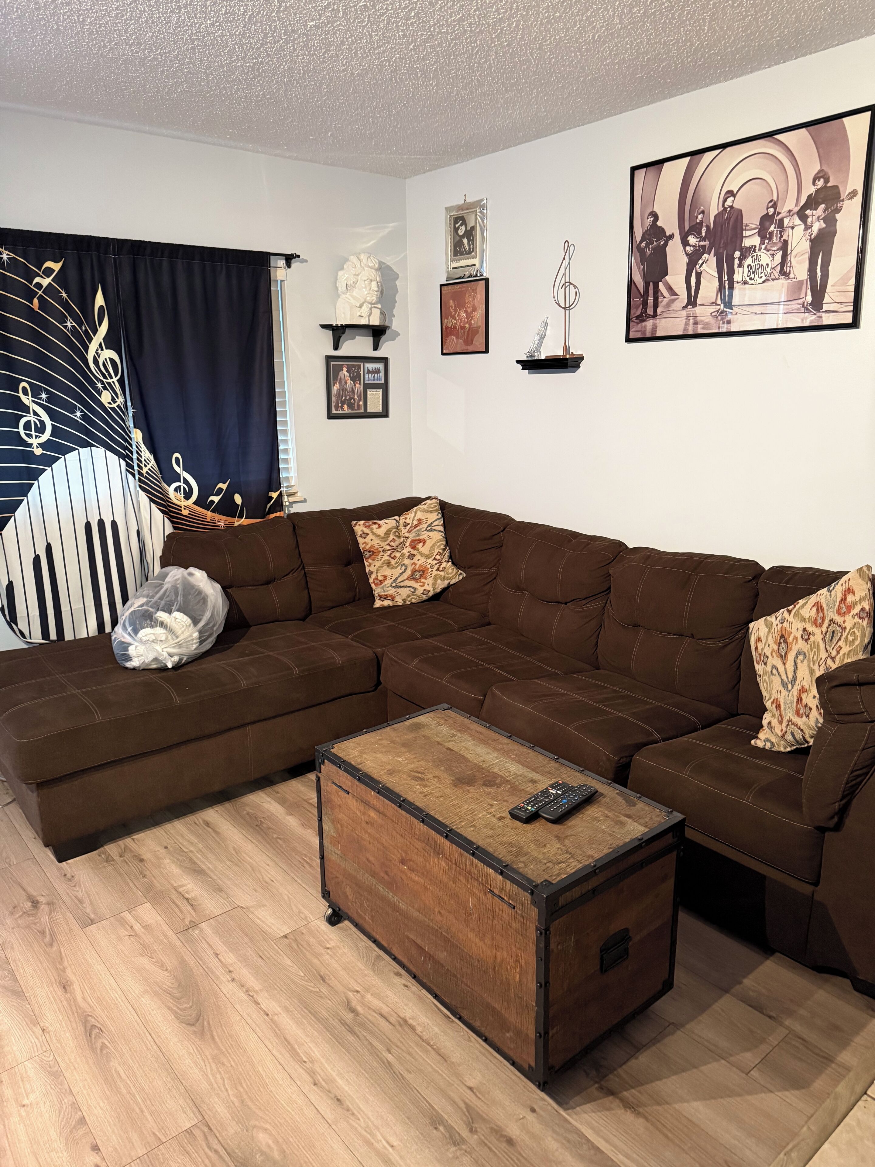 Una sala de estar con un sofá seccional marrón, una mesa de centro de madera y una cortina con notas musicales.
