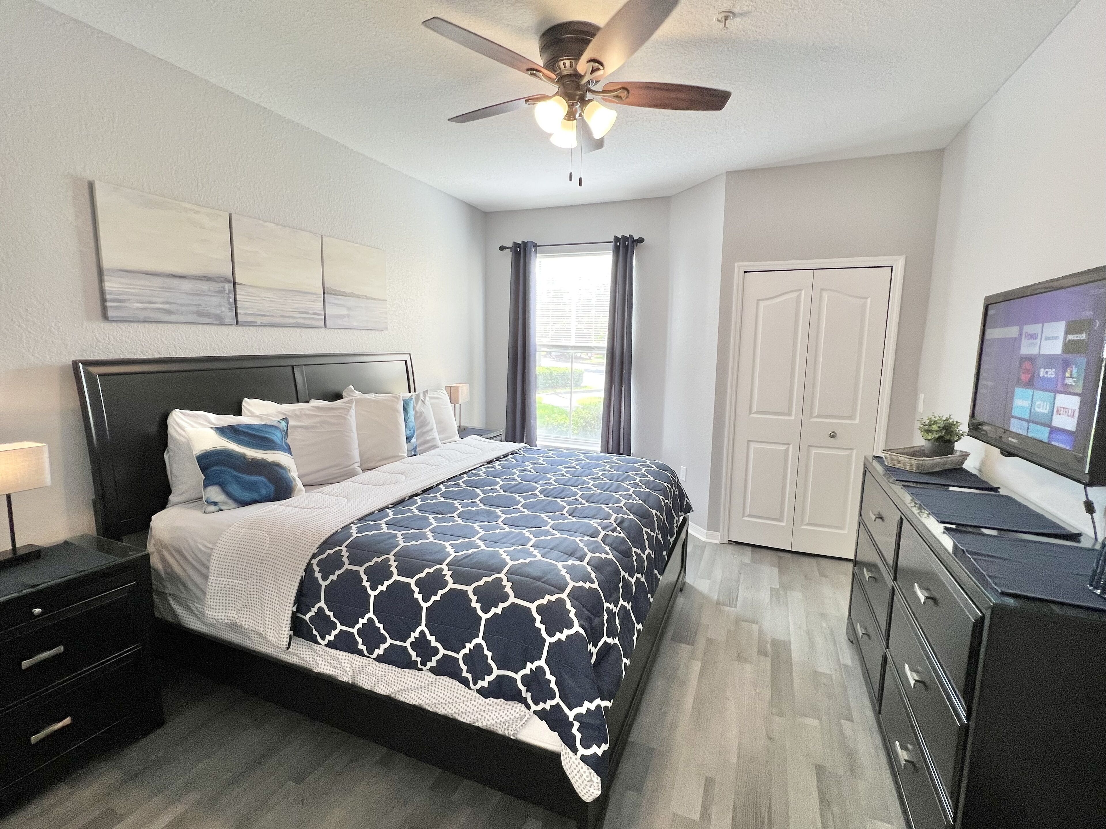 A bedroom with a bed, a ceiling fan, a TV, and a dresser.