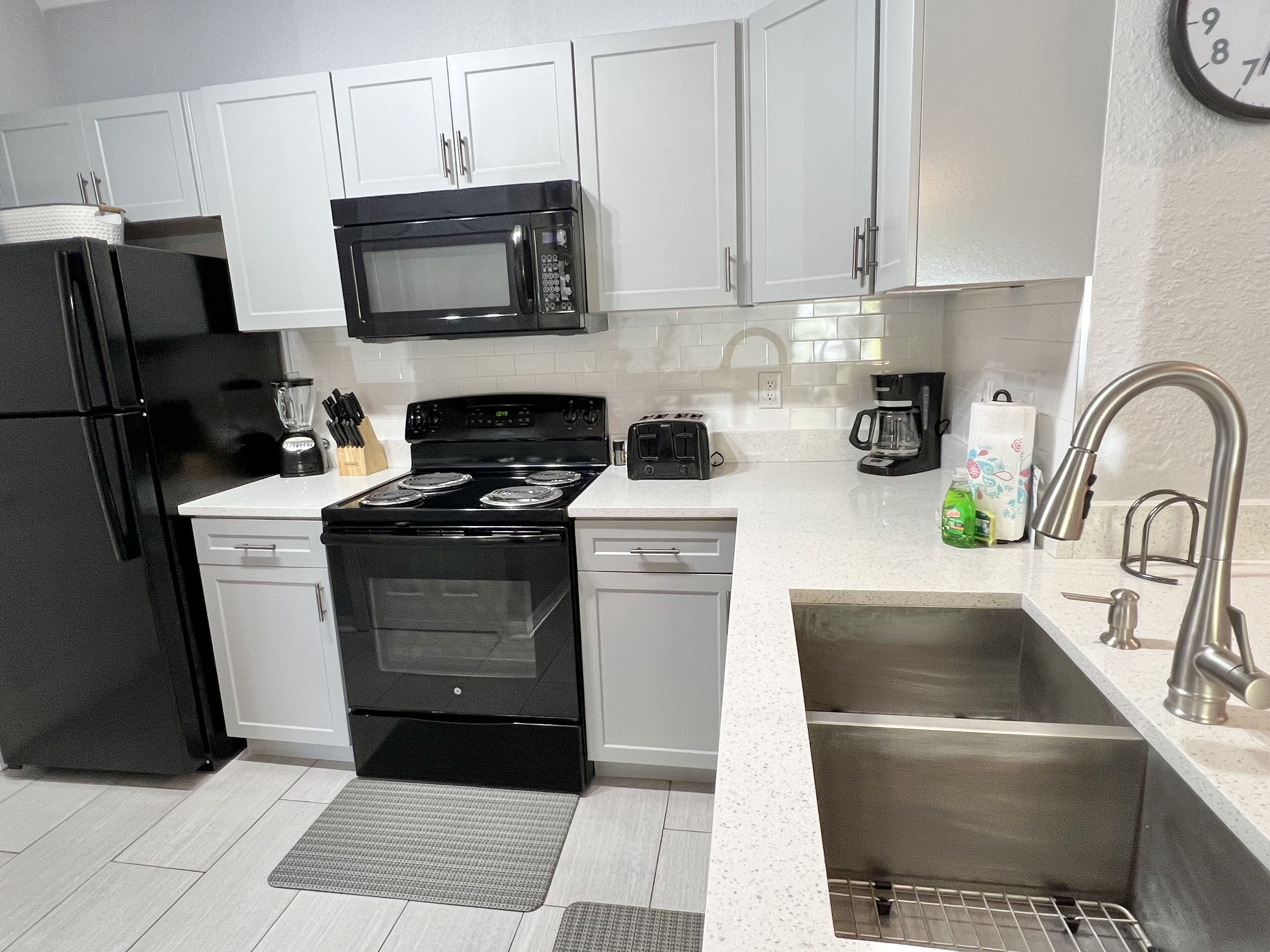 A modern kitchen with white cabinets, a black stove, a microwave, a refrigerator, a sink, and a toaster.