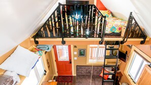 A loft-style bedroom with a bunk bed, a sofa, a ladder, and a small table. - Talkeetna Tiny House Cabin Denali Indoor Sauna/firepit/bike/ski/multi-use trails (Talkeetna)
