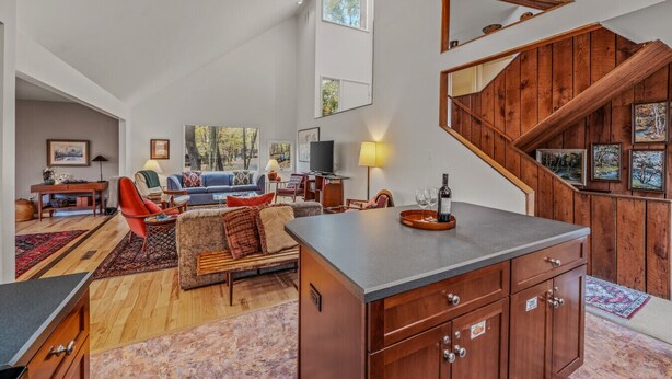 Amplia sala de estar con un ventanal grande, una escalera de madera y una zona de cocina con mostrador.