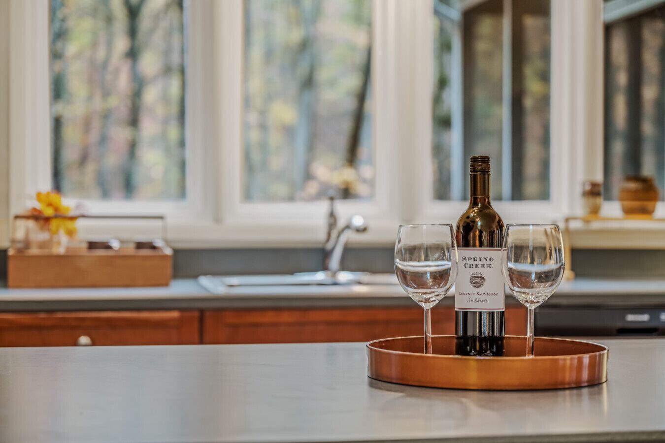 A kitchen counter with a wine bottle and two glasses on a copper tray.