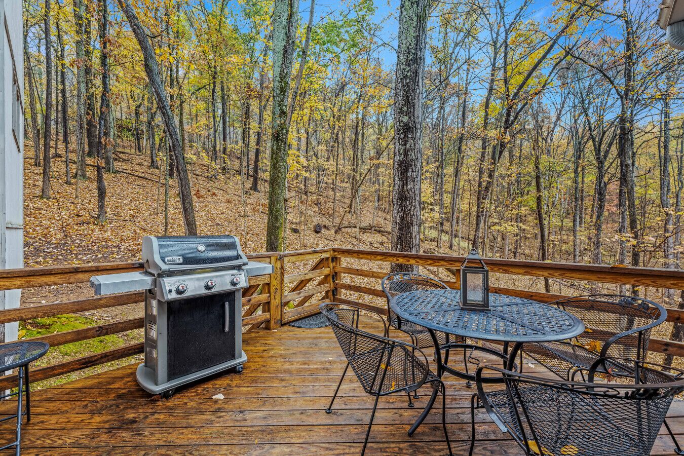 A deck with a grill, chairs, and a table overlooking a forest.