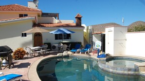 Une piscine avec des chaises longues et un espace barbecue.