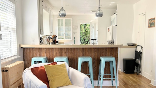 A modern kitchen with a central island, bar stools, and a white chair.