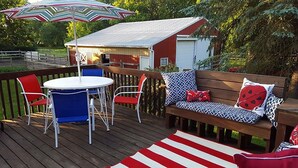 A wooden deck with a round table and chairs, a wooden bench with patterned cushions, and a striped rug. - The Farmhouse reopens after an upgrade on the second floor!   (South Bend)
