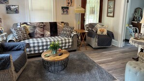 A cozy living room with a checkered sofa, a round coffee table, and a patterned armchair. - The Farmhouse reopens after an upgrade on the second floor!   (South Bend)