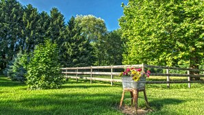 A rustic outdoor setting with a wooden fence, a metal bucket with flowers, and lush greenery. - The Farmhouse reopens after an upgrade on the second floor!   (South Bend)