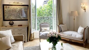 A well-lit room with a large window, a framed map, a globe, a sofa, a chair, and a table with a vase of flowers and a bottle. - Stylish & Sunny with Breath-taking Eiffel View, Perfect for Families (Paris)
