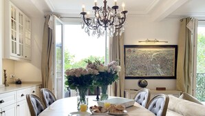 A dining area with a round table, chairs, a chandelier, a vase with flowers, and a framed map on the wall. - Stylish & Sunny with Breath-taking Eiffel View, Perfect for Families (Paris)