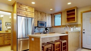 Una cocina con armarios de madera, electrodomésticos de acero inoxidable, microondas y una pequeña barra con taburetes.