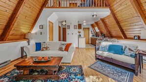 Ein Loft-Zimmer mit hohen Decken, Holzbalken, einem weißen Sofa, einem Holztisch und einem gemusterten Teppich.