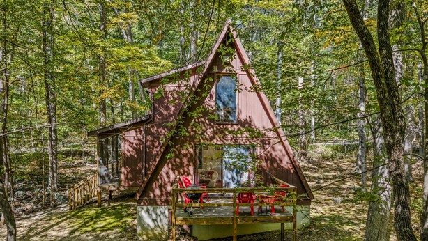 Eine Holzhütte mit einem dreieckigen Dach, einer Veranda mit roten Stühlen und einem kleinen Tisch.