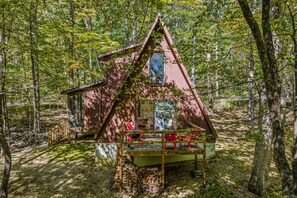Une cabane avec un toit triangulaire, une véranda avec des chaises rouges et une petite table.