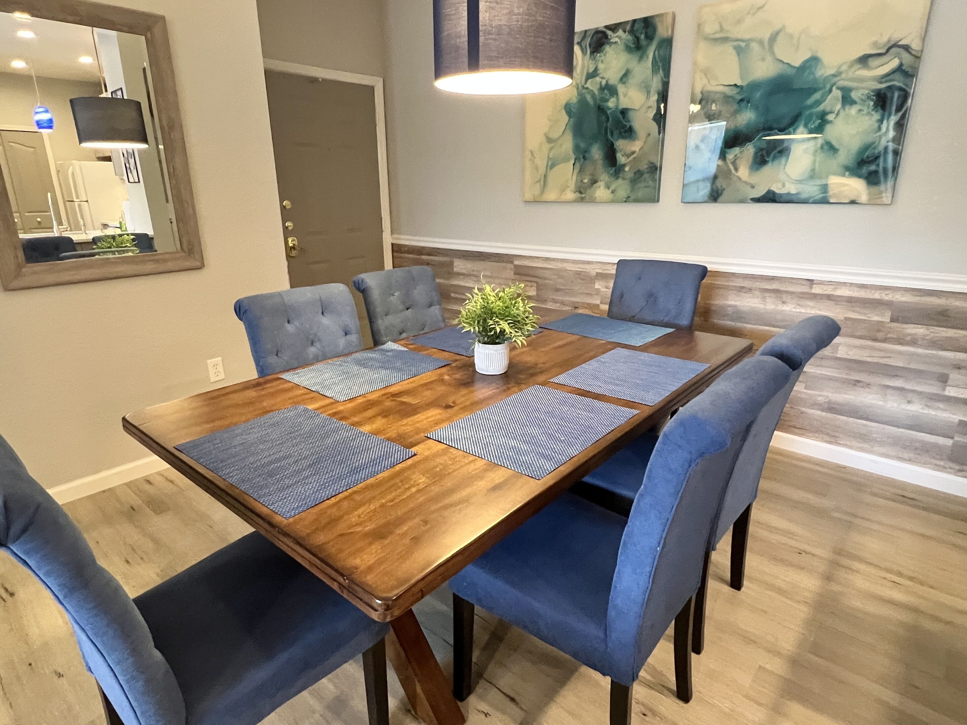Een eetruimte met een houten tafel, blauwe gestoffeerde stoelen en een potplant.