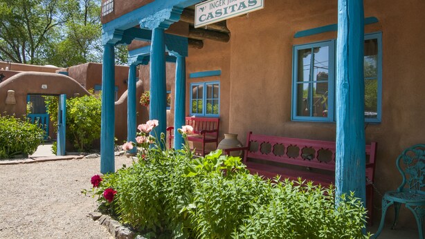 A building with a sign reading "INGER JIRBY'S CASITAS" and a porch with blue columns and a red bench. - Spacious, Sunlit Adobe Casita #6 / B&B in the Heart of Historic Taos! (Taos)