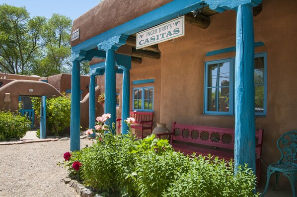 A building with a sign reading "INGER JIRBY'S CASITAS" and a porch with blue columns and a red bench. - Spacious, Sunlit Adobe Casita #6 / B&B in the Heart of Historic Taos! (Taos)