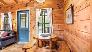 Un accogliente interno di una baita con arredamento in legno, un tavolo rotondo in legno con panche, un divano e una porta con tende.