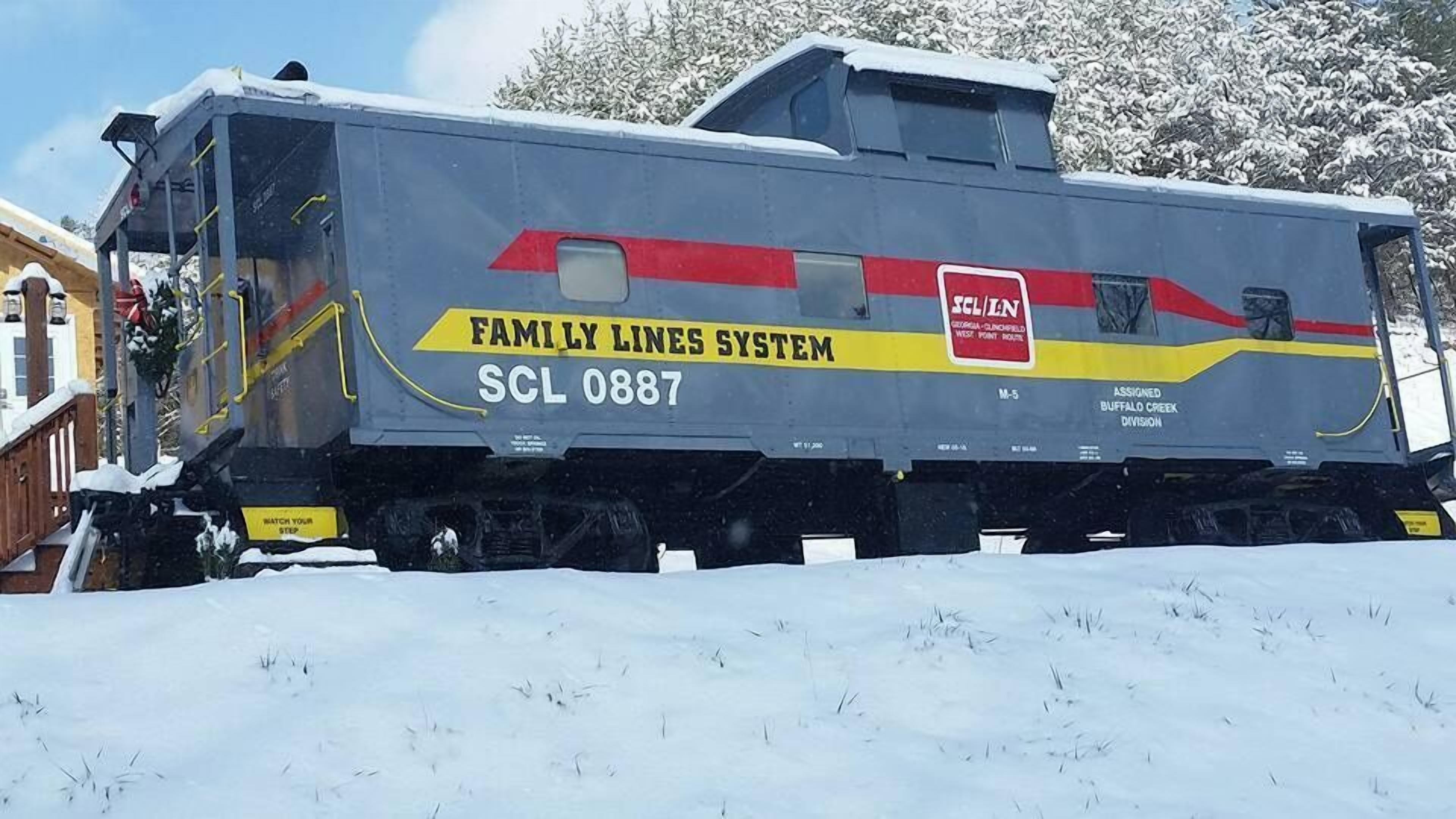 Ein Zug mit der Aufschrift 'Family Lines System' und 'SCL 0887', geparkt in einer verschneiten Gegend.