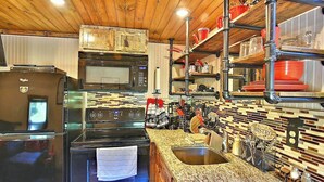 A kitchen with a microwave, oven, and sink. There are shelves with dishes and a sign that says 'BISTRO'.