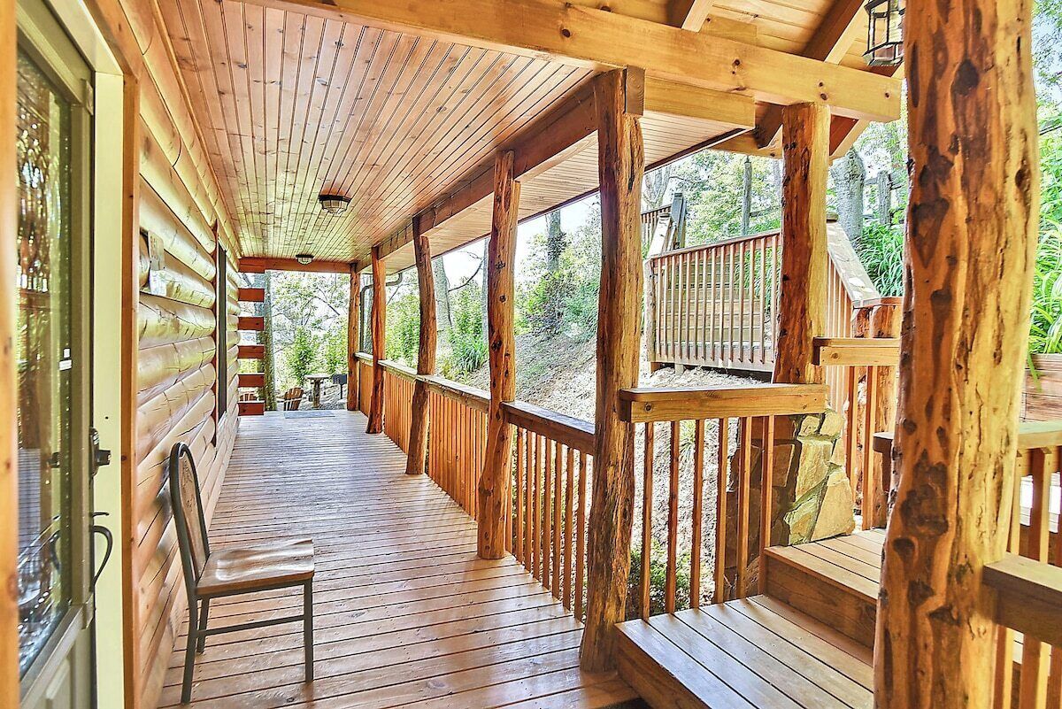 A wooden deck with a bench, wooden railings, and a view of the surrounding forest.
