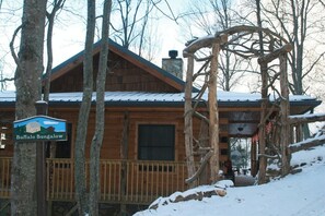 A wooden cabin with a covered porch, surrounded by trees and a snowy landscape.