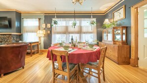 Une salle à manger avec une nappe rouge, des chaises en bois, un lustre et une cheminée en pierre.