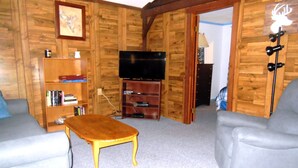 Una sala de estar acogedora con paredes de madera, un televisor de pantalla plana, una estantería y dos sofás grises.