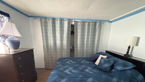 Un dormitorio con cama, cómoda, mesita de noche, lámpara y cortina.