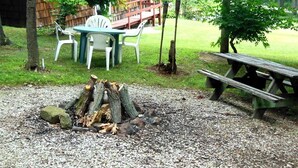 Un espacio de descanso al aire libre rústico con un brasero, una mesa de picnic y sillas.