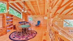 A wooden cabin interior with a dining table, chairs, a bookshelf, and a staircase.
