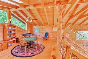 Interior de una cabaña de madera con una mesa de comedor, sillas, una estantería y una escalera.