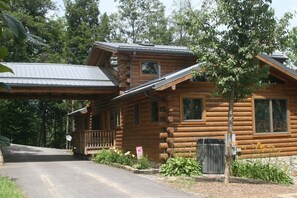 A log cabin with a porch, a satellite dish, and a stone wall. - Tatonka Lodge: 2 master suites on a bison ranch (Clyde)