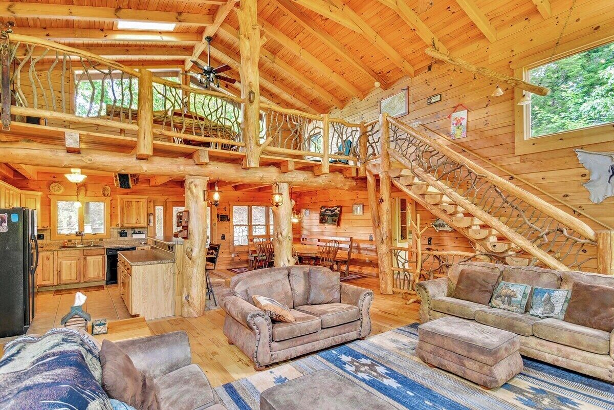 A spacious log cabin interior with a central living area, a kitchen, and a staircase leading to a loft.