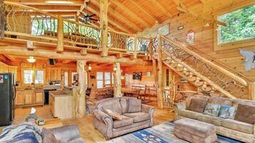 A spacious log cabin interior with a central living area, a kitchen, and a staircase leading to a loft.