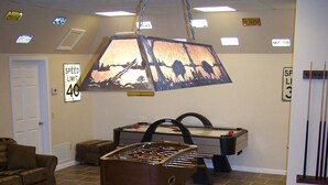 A pool table with balls, a foosball table, and a dog in a room with a ceiling light fixture.