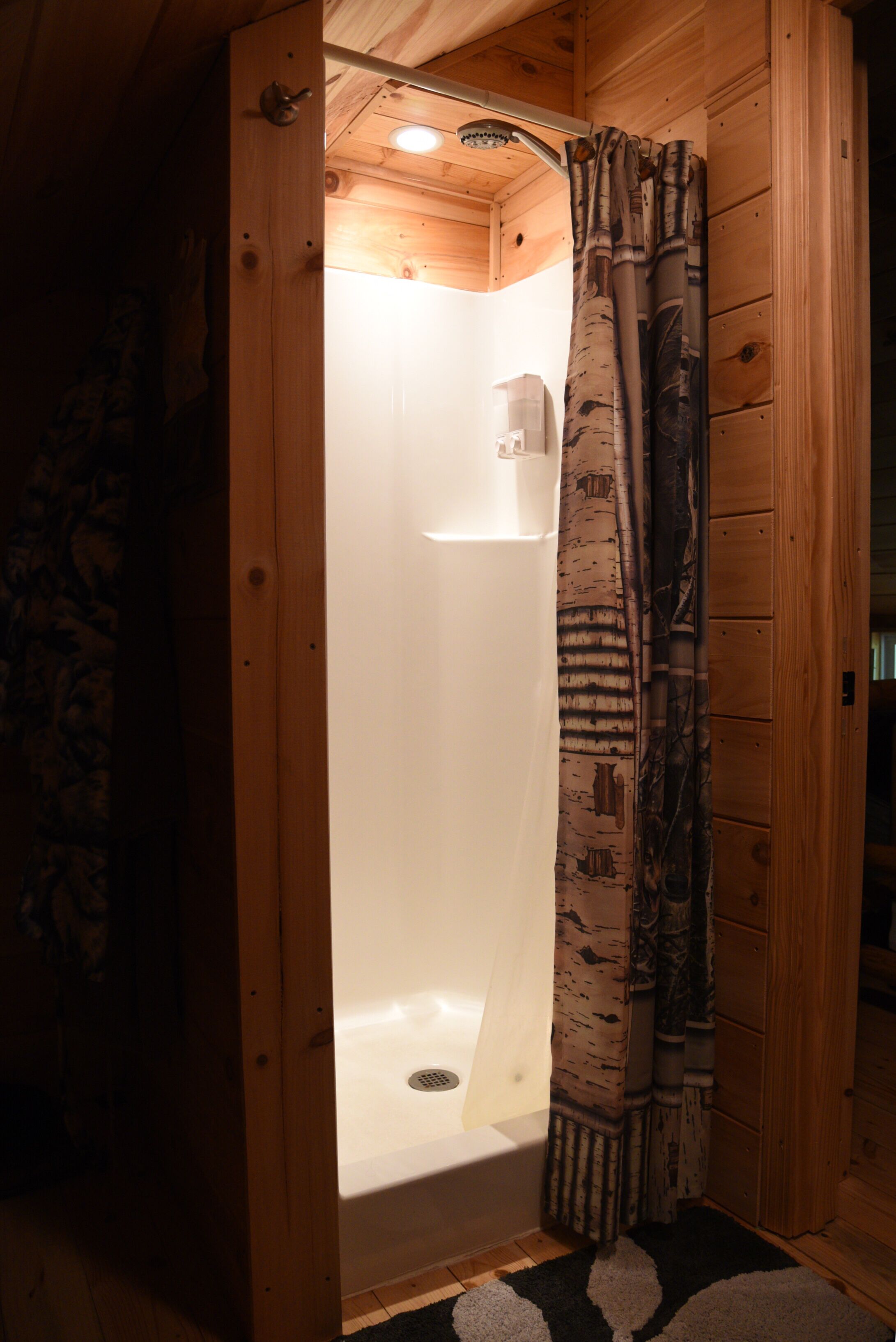 A wooden cabin bathroom with a shower, a white sink, and a patterned curtain.