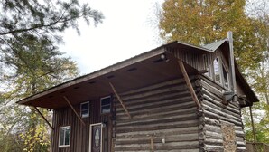 A rustic log cabin with a front porch, a chimney, and a small window.