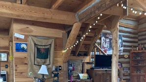 A rustic wooden interior with a dining table, chairs, a lamp, and a kitchen area.