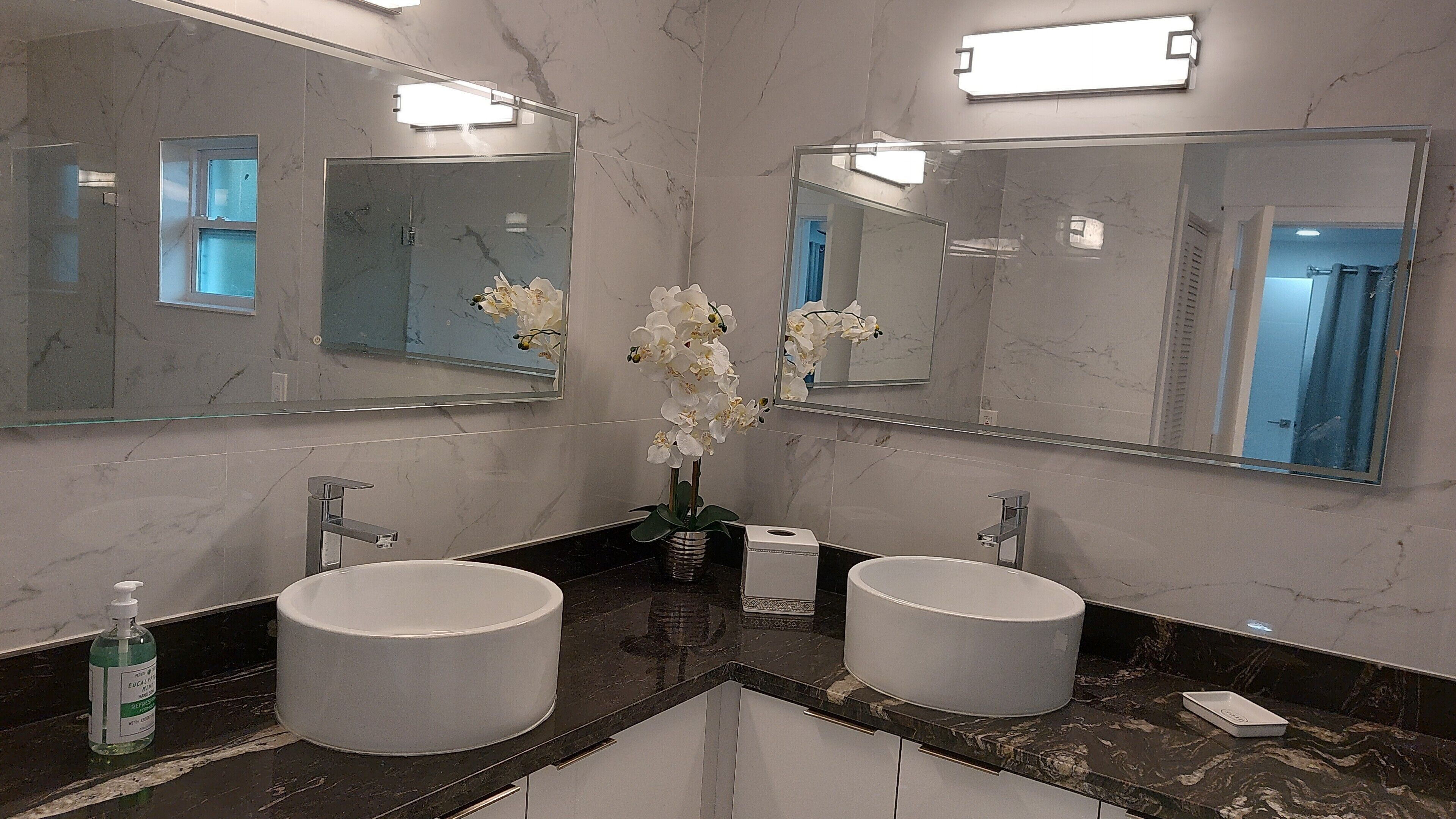 A bathroom with two sinks, a large mirror, and a vase with white flowers.