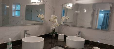 A bathroom with two sinks, a large mirror, and a vase with white flowers.