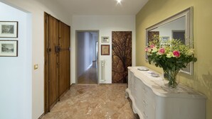 Un pasillo con suelo de mármol, puertas de madera, un tocador blanco con espejo y cuadros en la pared.