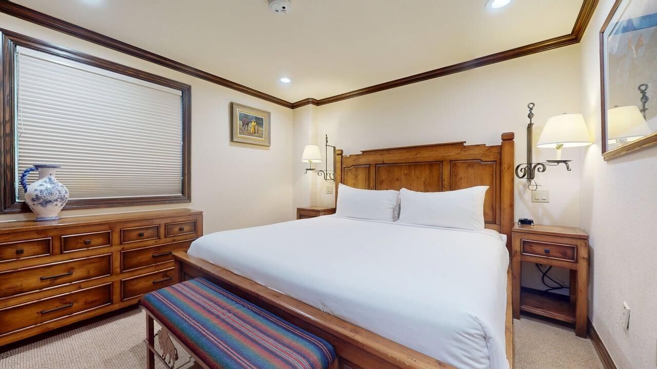 Una camera da letto con un letto grande, una testiera in legno, comodini con lampade, una panca, una cassettiera e una finestra con persiane.