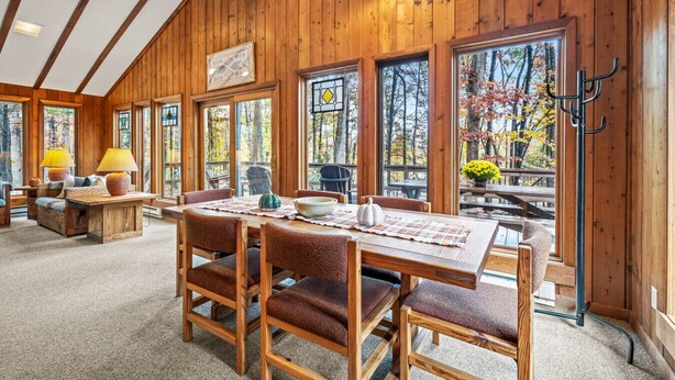 A wooden interior with a dining area, large windows, and a view of trees. - Haven Home - deck, grill, wifi, pool access, hiking, wood stove, games (Berkeley Springs)